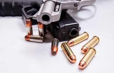 A snub nosed, stainless 357 magnum revolver on top of a black 9mm pistol with four bullets each caliber in front of them on a white background