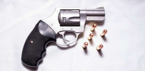 A stainless, snub nosed  357 magnum revolver with five full metal jacket bullets next to it on a...