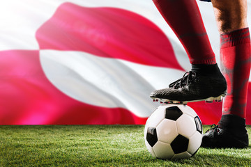 Close up legs of Greenland football team player in red socks, shoes on soccer ball at the free kick...