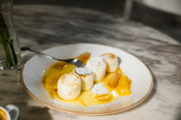 Cottage cheese pancakes with orange jam on white plate, marble table, at restaurant. Natural light and shadow food photography concept