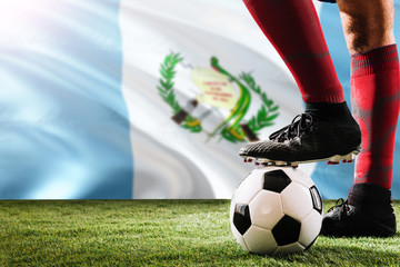 Close up legs of Guatemala football team player in red socks, shoes on soccer ball at the free kick or penalty spot playing on grass.