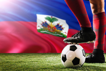 Close up legs of Haiti football team player in red socks, shoes on soccer ball at the free kick or penalty spot playing on grass. © sezerozger
