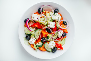 Greek salad with fresh tomato, cucumber, red onion, basil, lettuce, feta cheese, black olives and Italian herbs. Top view