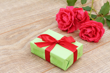 Gift box with rose flowers on the wooden background.