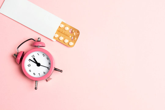 Female oral contraceptive pills blister with alarm clock on pink background. Women contraceptive hormonal birth control pills.