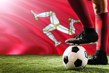 Close up legs of Isle Of Man football team player in red socks, shoes on soccer ball at the free kick or penalty spot playing on grass.