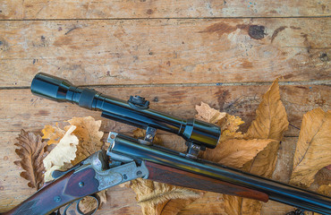 Beautiful hunting carbine with optical sight on the old wooden background with dry oak leaves and copy space