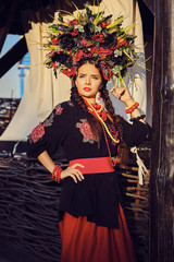 Brunette girl in a white ukrainian authentic national costume and a wreath of flowers is posing against a terrace. Close-up.