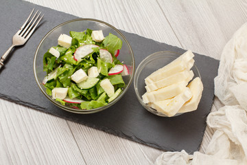 Fresh vegetable salad with cheese, cucumber and radish on stone board.