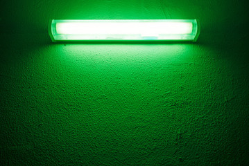 Green fluorescent lamp on a rough cement wall.