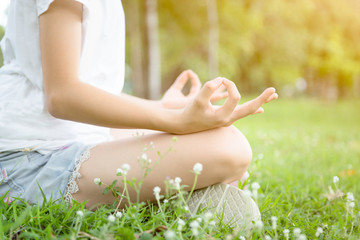 Closeup of woman hands meditating in yoga pose or lotus position on green grass,asian child girl practicing yoga meditation in outdoor park,relax time,calmness,meditation in nature,healthcare concept