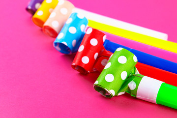 Multicolor party blowers on pink background. Multicolored party whistles. Decor for a birthday.