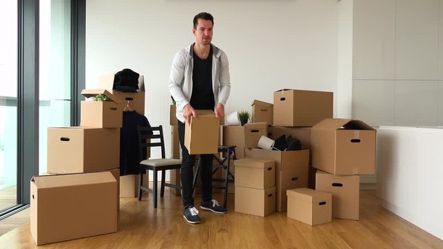 A moving man throws cardboard boxes to someone off the camera in an empty apartment