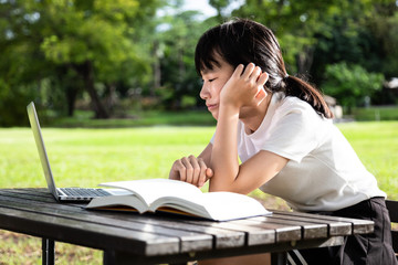 Asian child girl feeling boring while cramming,studying online,student with laptop computer and a book on table,schoolgirl is tired,exhausted while doing her school homework,education,laziness,bored 