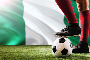 Close up legs of Nigeria football team player in red socks, shoes on soccer ball at the free kick or penalty spot playing on grass.