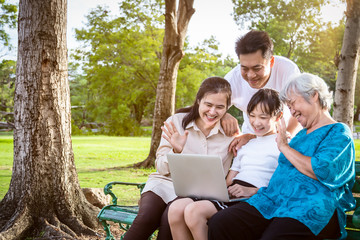 Happy asian family,father,mother,daughter enjoy smiling and senior grandmother with laptop computer,parent,child girl, having video call,talking,saying hi at park,communication,technology concept