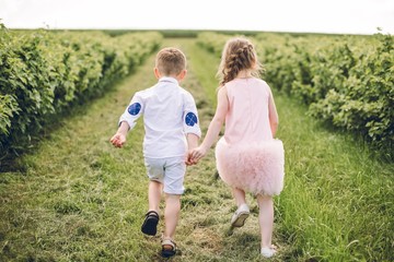 A boy and a girl in a pink dress run along the field with balloons in their hands