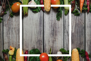 Creative layout made of corn, tomatoes, zucchini, carrot, beetroot, garlic, bean and white frame on wooden background. Food concept. Flat lay, top view. Free space for your text.