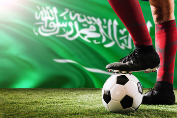 Close up legs of Saudi Arabia football team player in red socks, shoes on soccer ball at the free kick or penalty spot playing on grass.