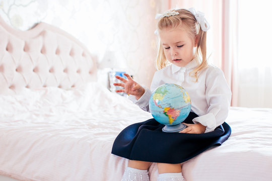 Little adorable blonde girl in school uniform and white golfs siting on a ber in her bedroom and shockes about first day in the school