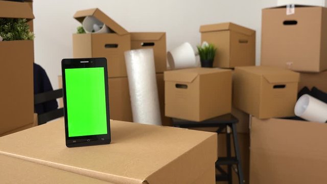 Closeup on a smartphone with green screen among cardboard boxes