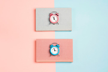 Blue and pink books with alarm clocks on a blue and pink background.
