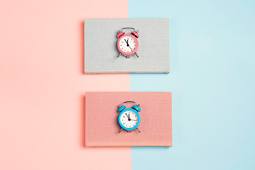 Blue and pink books with alarm clocks on a blue and pink background.