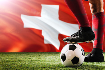 Close up legs of Switzerland football team player in red socks, shoes on soccer ball at the free kick or penalty spot playing on grass.
