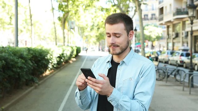 Man using smart phone and saying yes looking at camera in the street