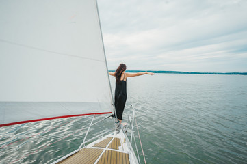 Young woman in black dress enjoying the beauty of the nature on sailing yacht sailing the sea.
