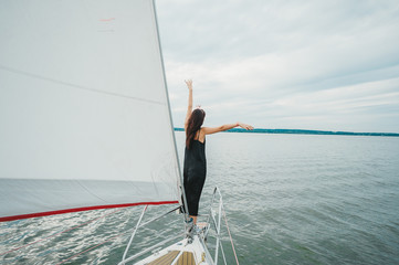 Beautiful young woman standing on the bow of a sail boat on a tranquil calm blue sea