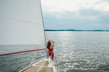 Young woman sitting at front of private luxury sailing yacht at sea. Rear view