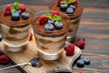Classic tiramisu dessert with blueberries and strawberries in a glass cup on cutting board on wooden background