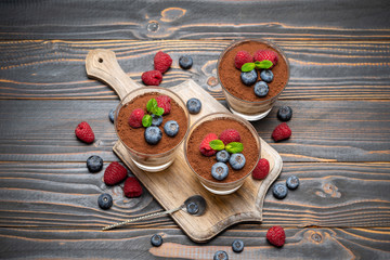 Classic tiramisu dessert with blueberries and strawberries in a glass cup on cutting board on wooden background