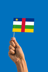 Woman hand holding Central African Republic flag with stick, waving flag on deep blue sky. National theme, deep blue sky.