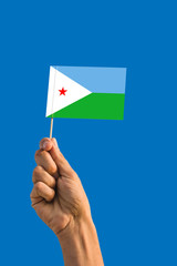 Woman hand holding Djibouti flag with stick, waving flag on deep blue sky. National theme, deep blue sky.