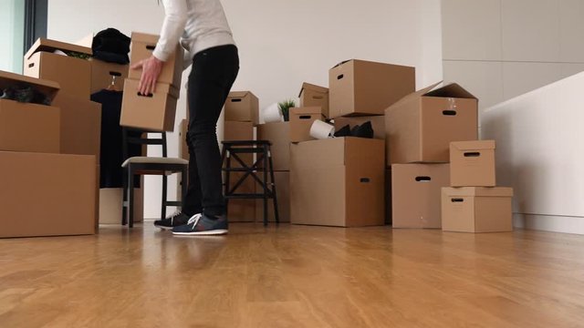 A moving man adds a cardboard box to a pile of other boxes in an empty apartment