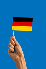 Woman hand holding Germany flag with stick, waving flag on deep blue sky. National theme, deep blue sky.