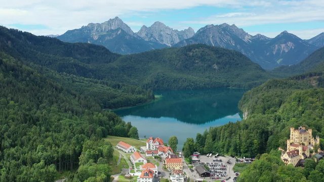 Aerial view of Hohenschwangau Castle in summer, picturesque palace in Bavarian Alps mountains, lush green hills and blue sky, lake Alpsee - landscape panorama of Bavaria from above, Germany, Europe