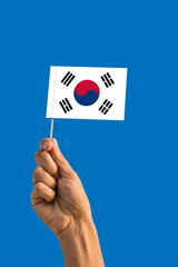 Woman hand holding South Korea flag with stick, waving flag on deep blue sky. National theme, deep blue sky.