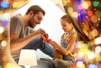 family, hygge and people concept - happy father and little daughter playing tea party in kids tent at night at home