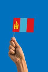 Woman hand holding Mongolia flag with stick, waving flag on deep blue sky. National theme, deep blue sky.