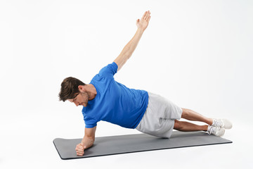 Concentrated serious strong young sports man on fitness rug isolated over white wall background make exercise.