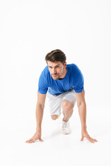 Handsome serious strong young sports man runner isolated over white wall background ready to run.