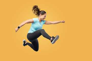 fitness, sport and people concept - happy smiling young woman jumping in air over yellow background