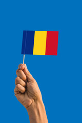 Woman hand holding Romania flag with stick, waving flag on deep blue sky. National theme, deep blue sky.