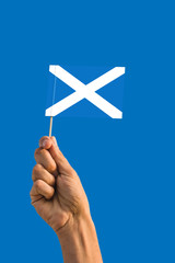 Woman hand holding Scotland flag with stick, waving flag on deep blue sky. National theme, deep blue sky.