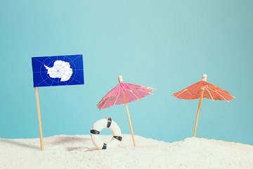 Miniature flag of Antarctica on beach with colorful umbrellas and life preserver. Travel concept, summer theme.