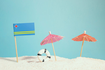 Miniature flag of Aruba on beach with colorful umbrellas and life preserver. Travel concept, summer theme.
