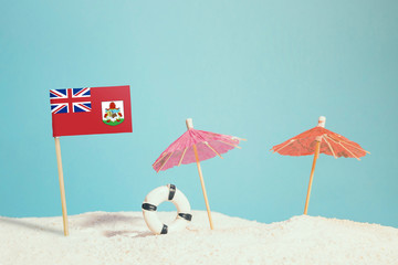 Miniature flag of Bermuda on beach with colorful umbrellas and life preserver. Travel concept, summer theme.